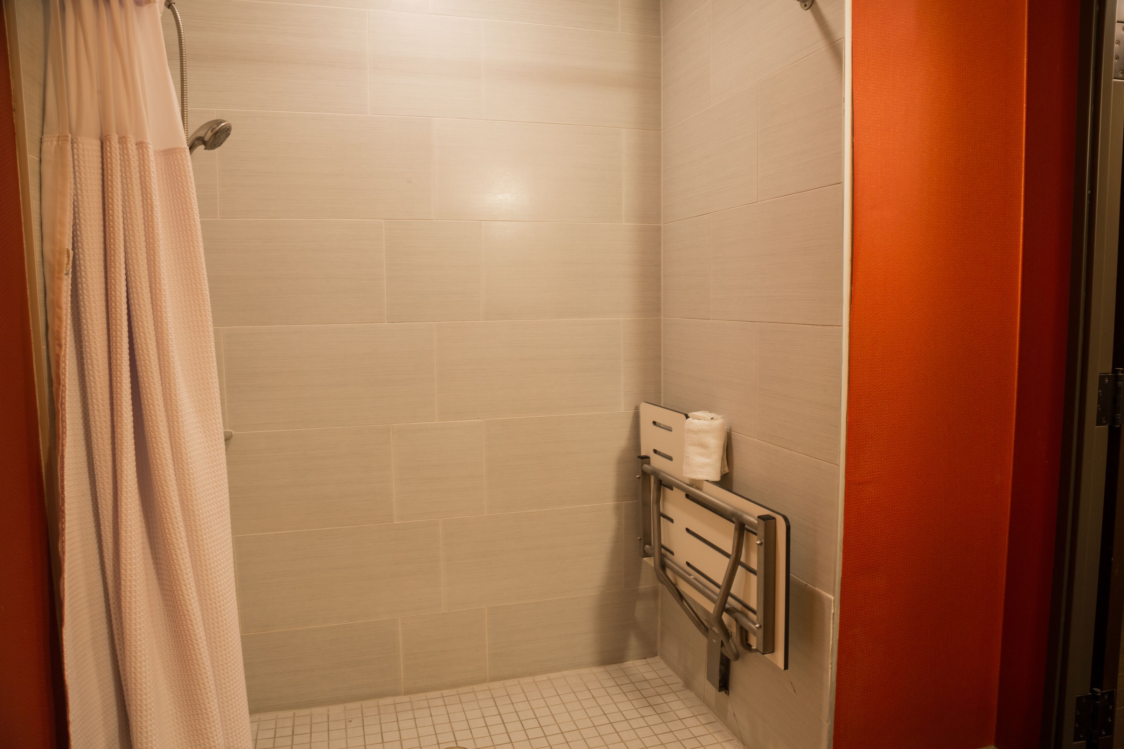 Un petit espace de douche fermé, avec des murs carrelés, une pomme de douche et une barre d’appui.