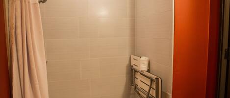 Un petit espace de douche fermé, avec des murs carrelés, une pomme de douche et une barre d’appui.