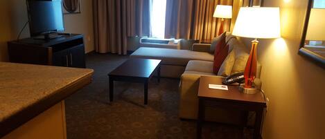 A hotel room with a sofa, a small table, a TV on a stand, a lamp, and a telephone on a bedside table.