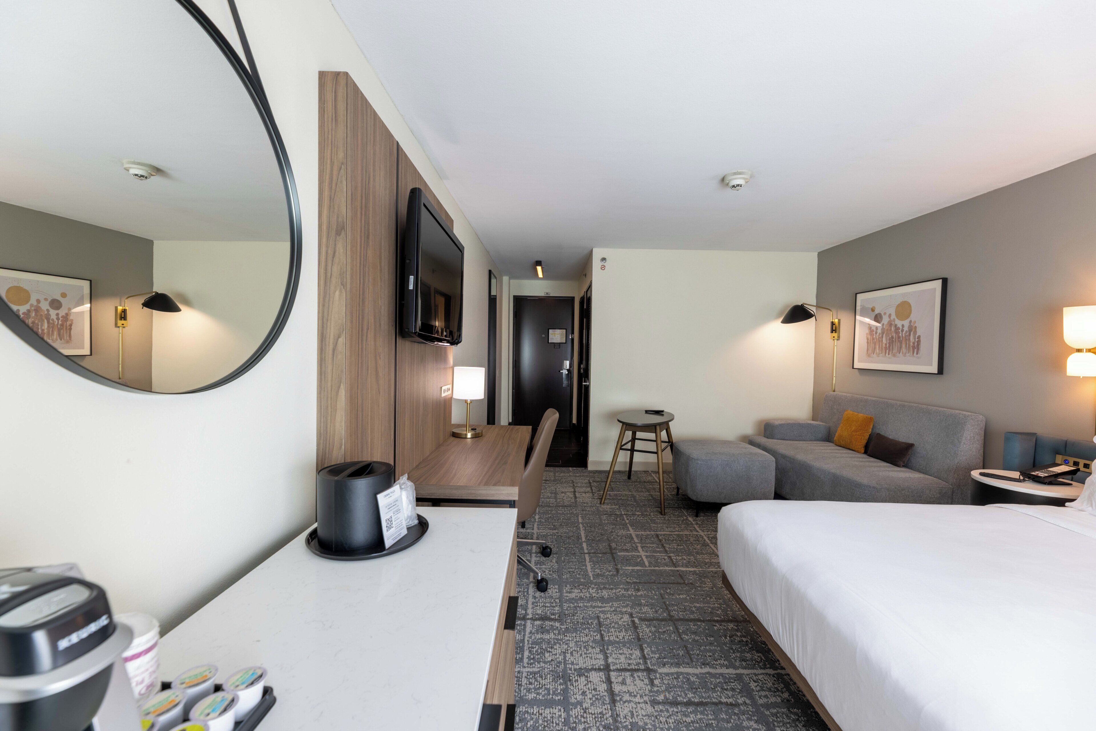Une chambre d’hôtel comprenant un lit, un bureau avec une machine à café, une télévision, un canapé et une petite table avec une lampe.