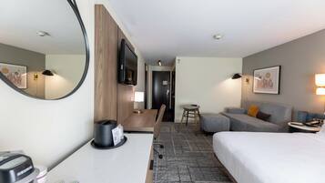 Une chambre d’hôtel comprenant un lit, un bureau avec une machine à café, une télévision, un canapé et une petite table avec une lampe.