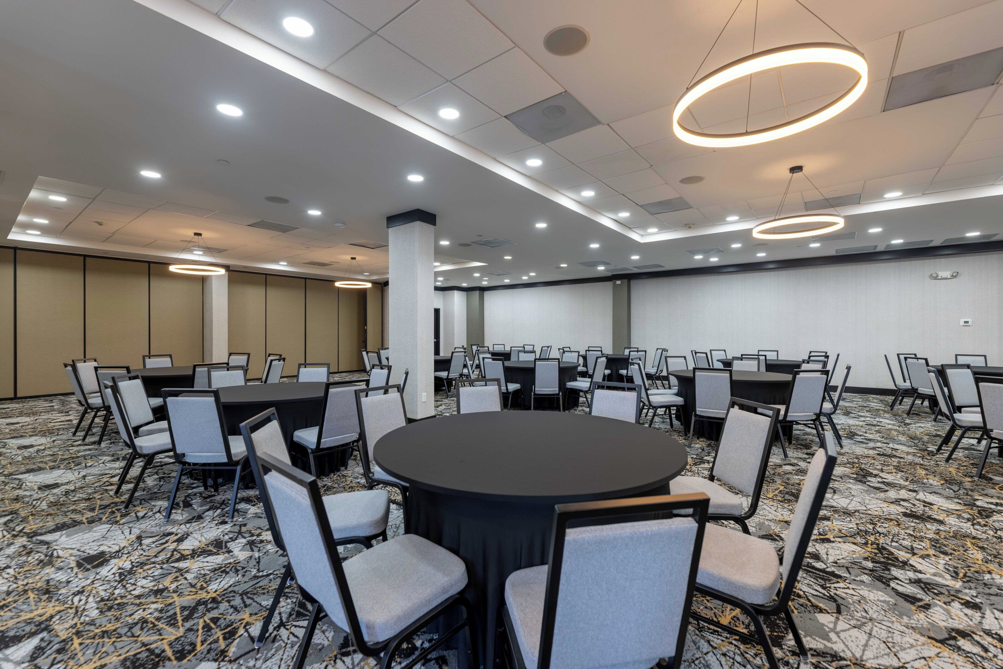 A conference room with round tables and chairs, recessed lighting, and a patterned carpet.