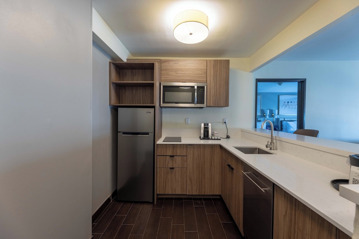 A modern kitchen with wooden cabinets, a stainless steel refrigerator, a microwave, and a dishwasher.