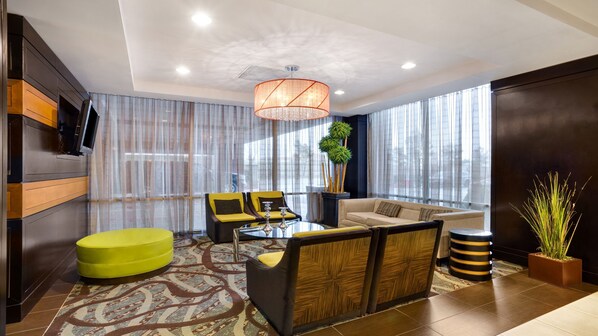 A modern living room with a sofa, armchair, and ottoman, a coffee table, and a large window with curtains. - Crowne Plaza Houston Galleria Area by IHG (Houston)