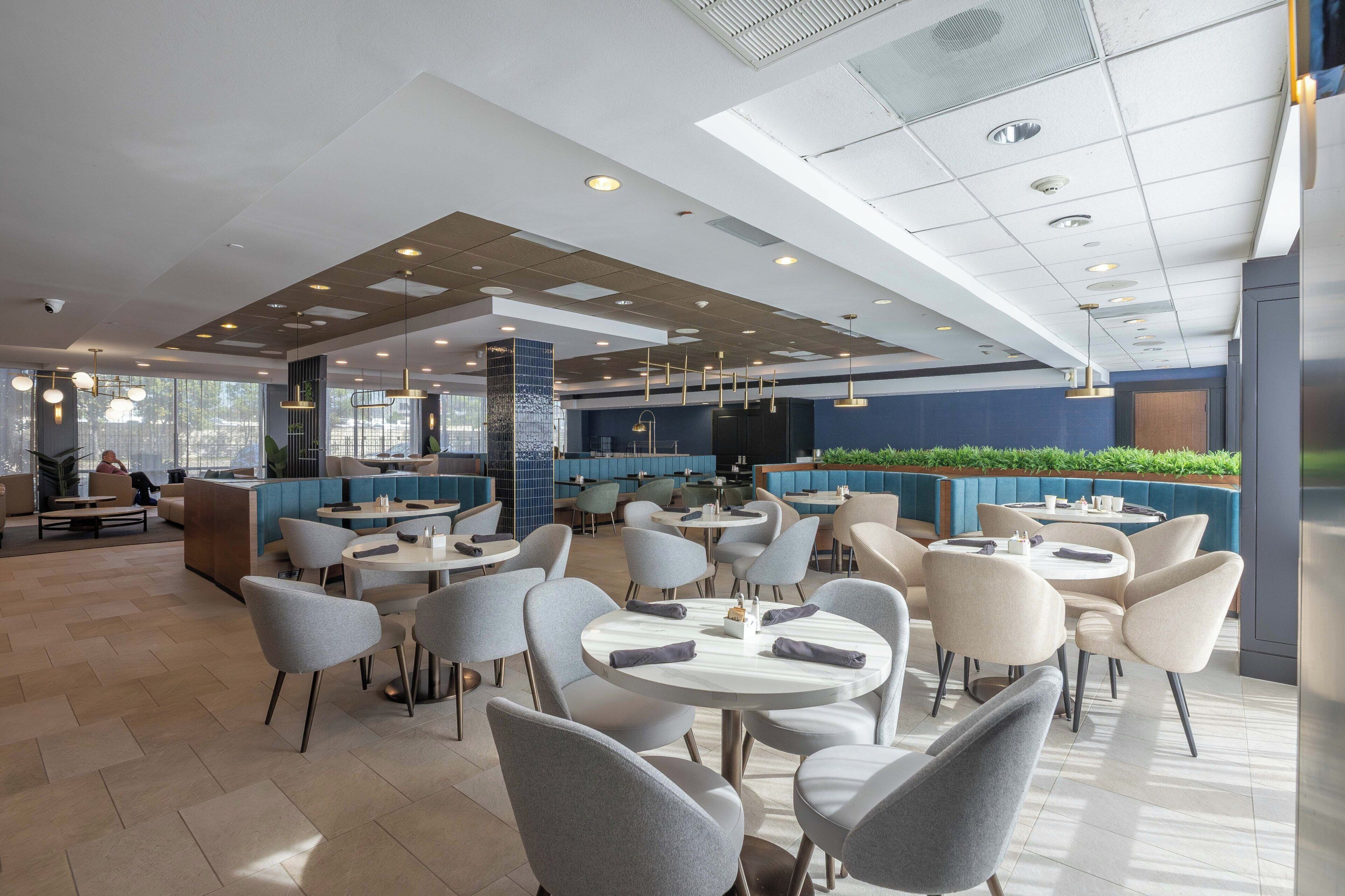 Ein modernes Restaurant mit runden Tischen und Stühlen, einer Bar und einer Sitzgelegenheit mit Sofas und einem hohen Tisch.
