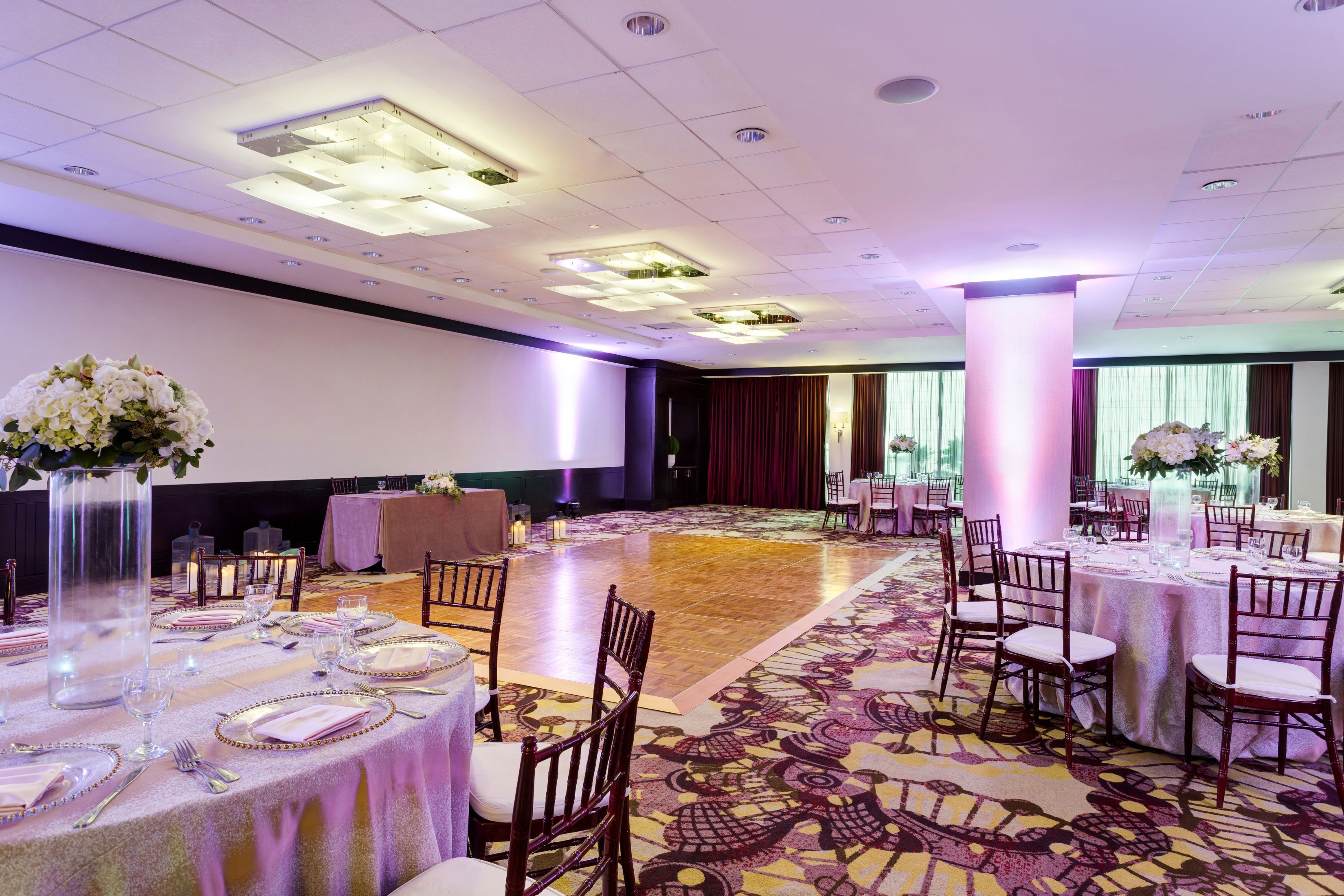 A banquet hall with round tables set for dining, large floral centerpieces, and a patterned carpet.