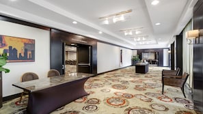 A spacious hotel corridor with a long conference table, chairs, and a patterned carpet.