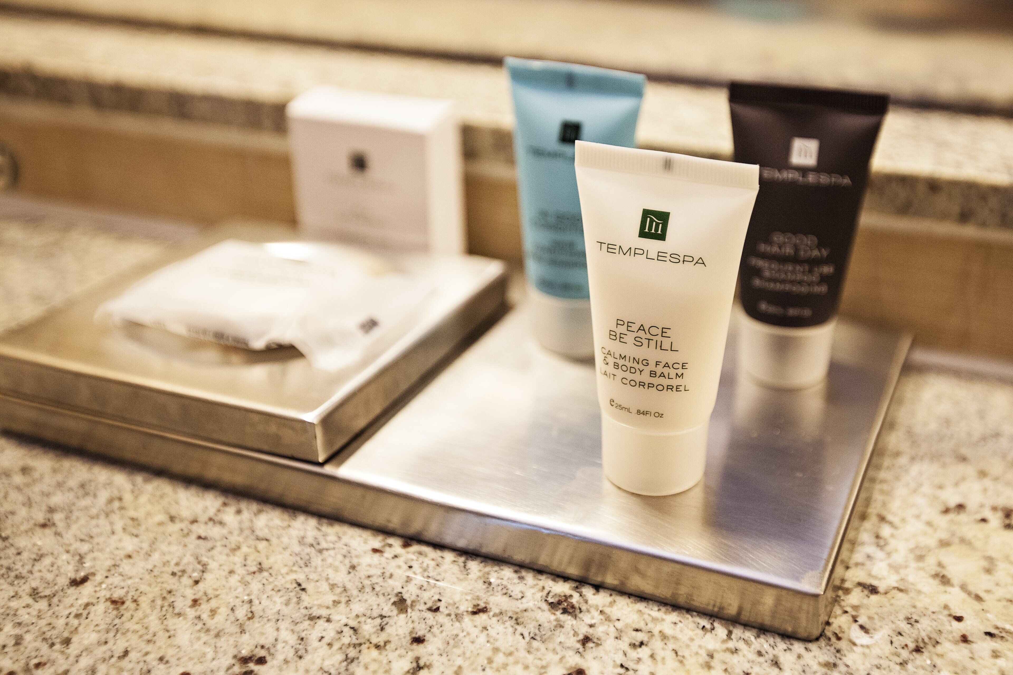 A bathroom counter with a soap dispenser, a tube of lotion, and a blue bottle, possibly a shampoo or conditioner.