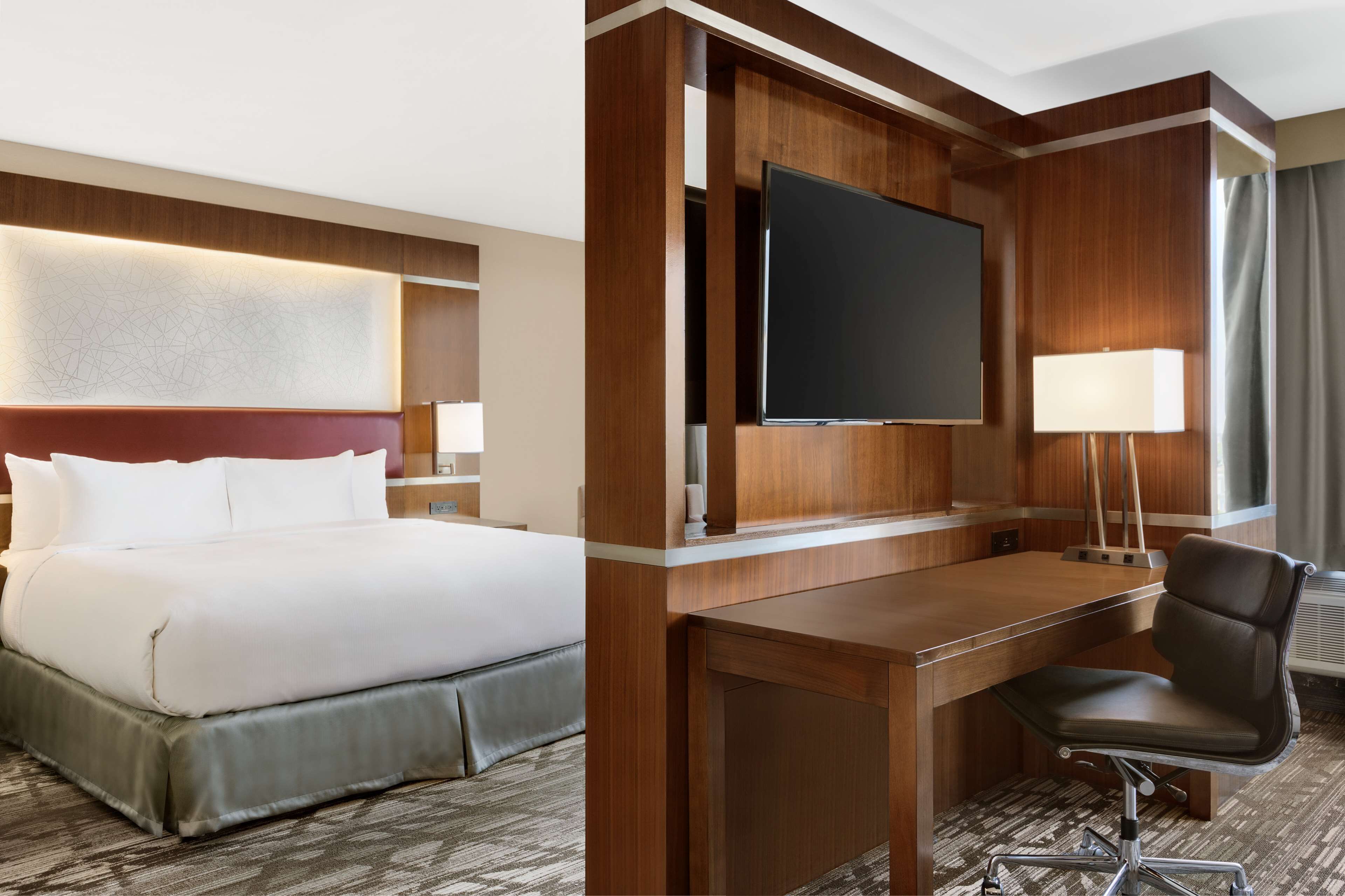 A hotel room with a bed, a desk, a chair, a flat-screen TV, and a lamp.