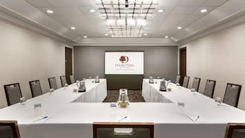 Un salón de conferencias con una mesa larga, sillas y una pantalla proyectora mostrando el logotipo de DoubleTree.