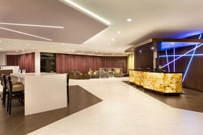 Welcome to our hotel lobby, featuring a central reception desk and comfortable seating area with a sofa and armchairs.
