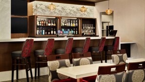 Zona de bar con mostrador, estanterías llenas de botellas y taburetes con cojines estampados.