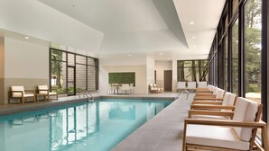 Una piscina interior con sillones de descanso y vistas a árboles a través de grandes ventanales.
