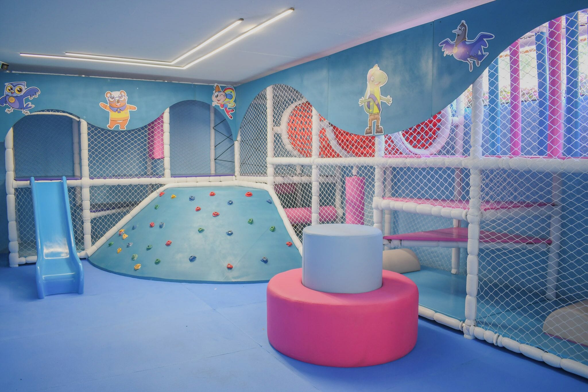 Zona de juegos infantiles con tobogán, pared de escalar y estructuras de juego acolchadas.