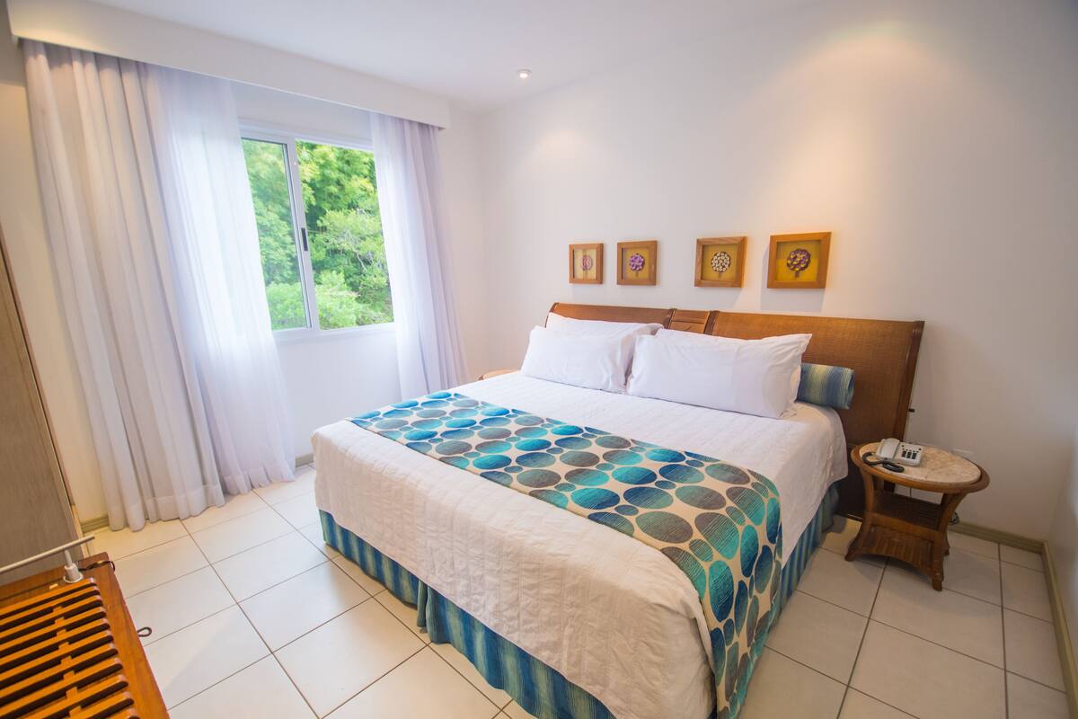 A hotel room with a bed, a bedside table with a phone, and a window with curtains.