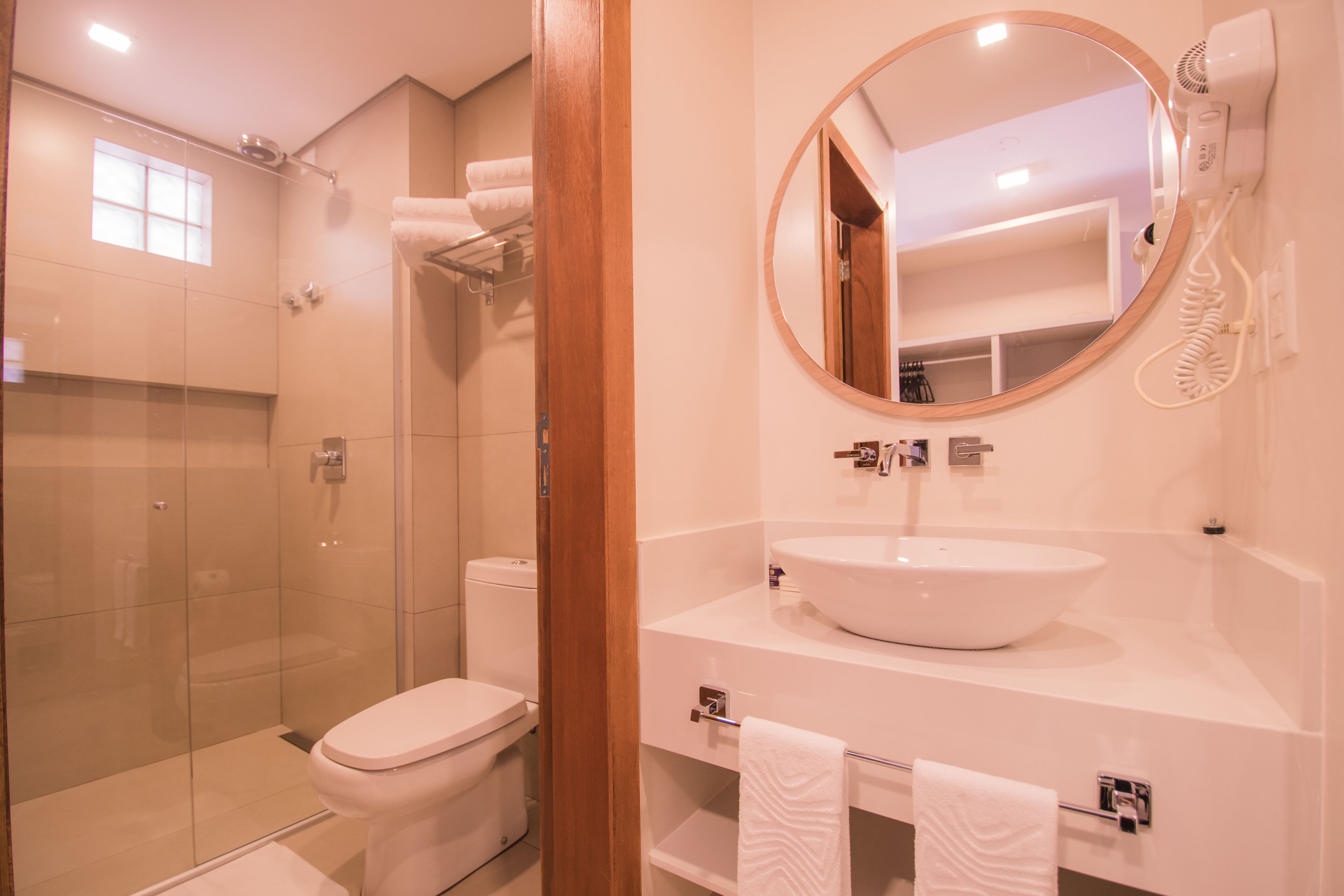 Un baño moderno con ducha acristalada, inodoro blanco, espejo redondo y lavamanos blanco.