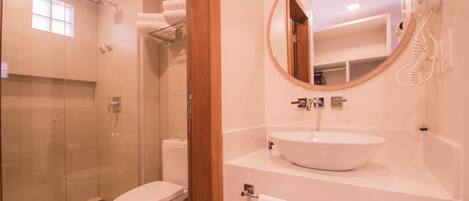 Un baño moderno con ducha acristalada, inodoro blanco, espejo redondo y lavamanos blanco.