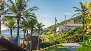 A tropical resort with palm trees, a beach, and a building with a thatched roof. - Costao do Santinho Resort - All Inclusive (Florianópolis)