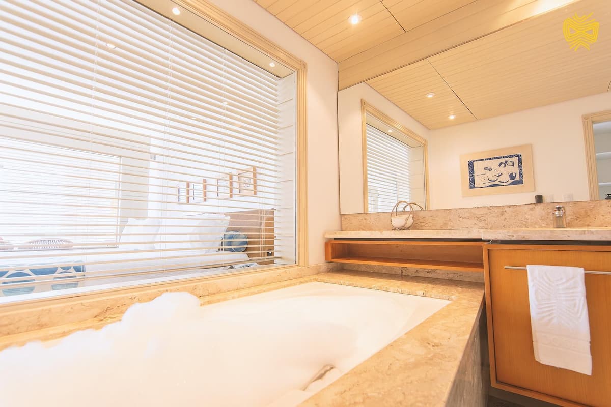 A modern bathroom with a large bathtub, wooden vanity, and a window with blinds.