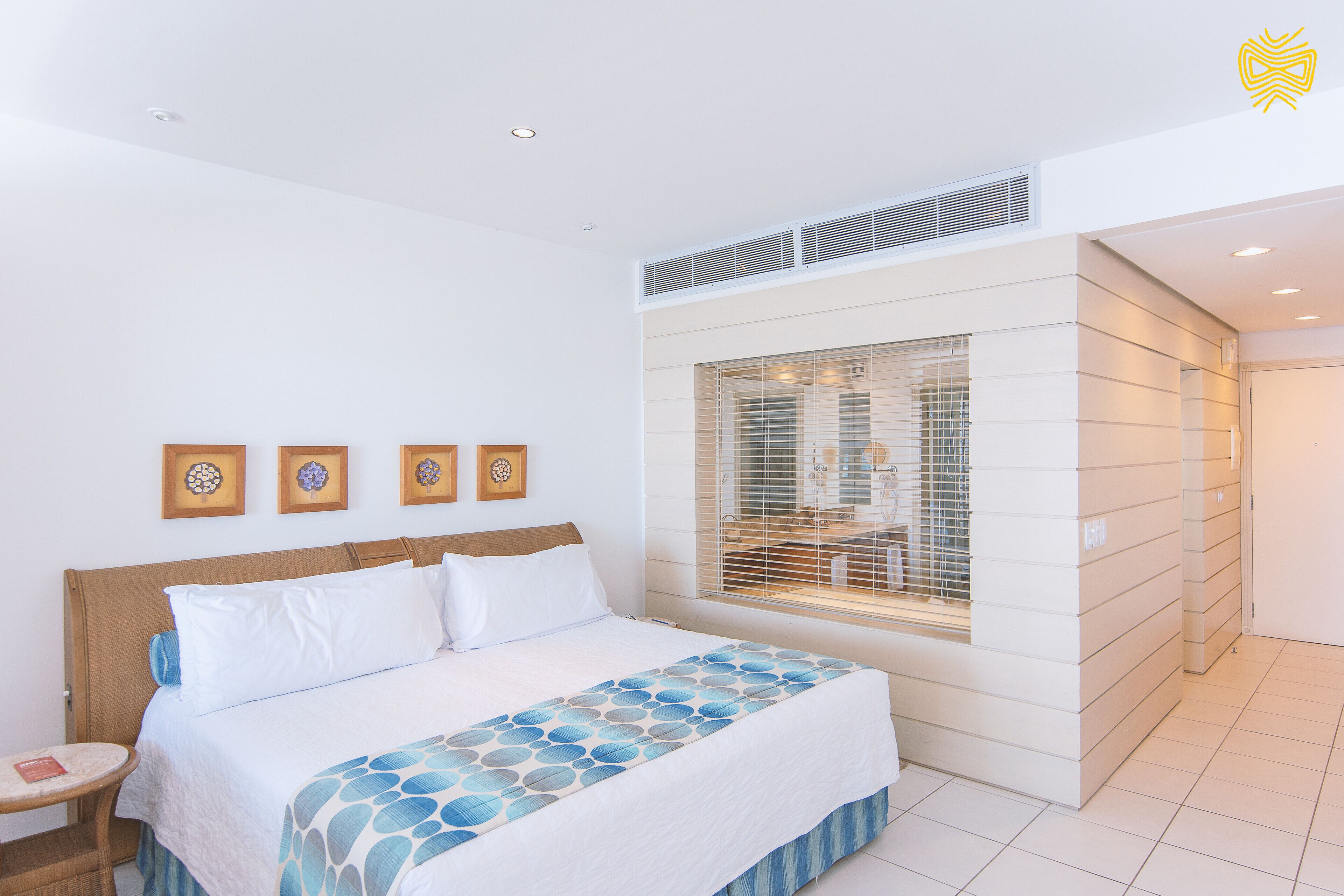 Habitación de hotel moderna con una cama grande, una mesita de noche pequeña, una ventana con persianas y vistas al exterior.