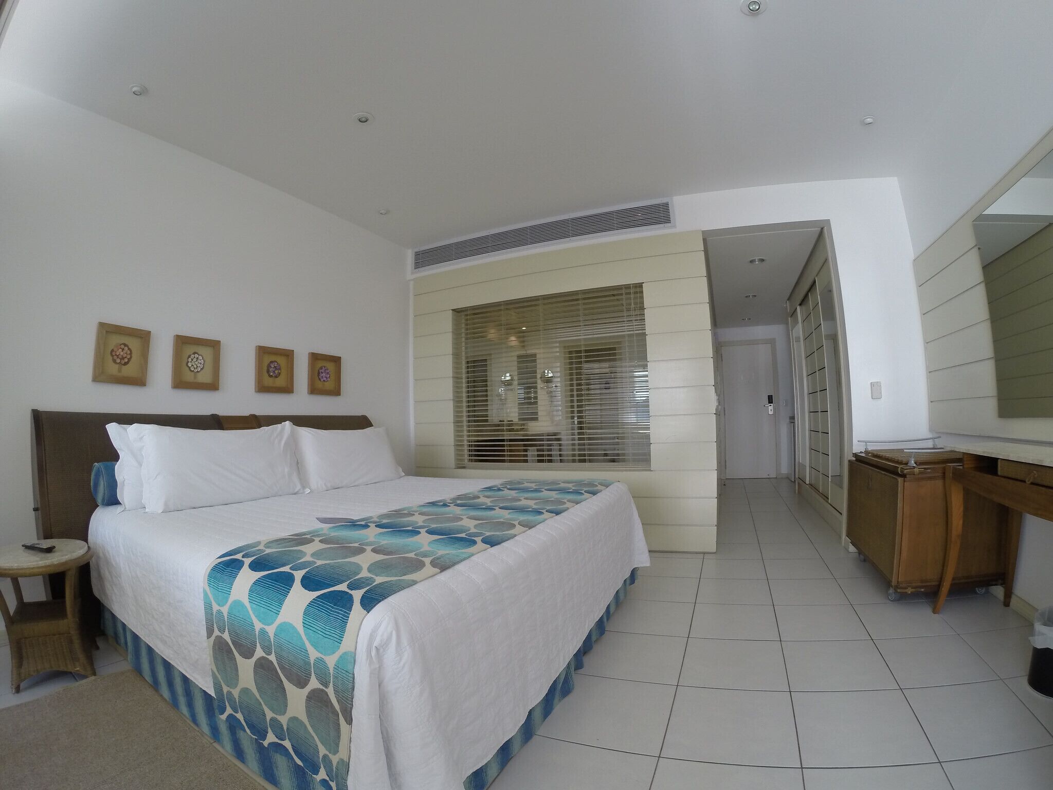 A hotel room with a bed, bedside table, and a desk with a mirror.