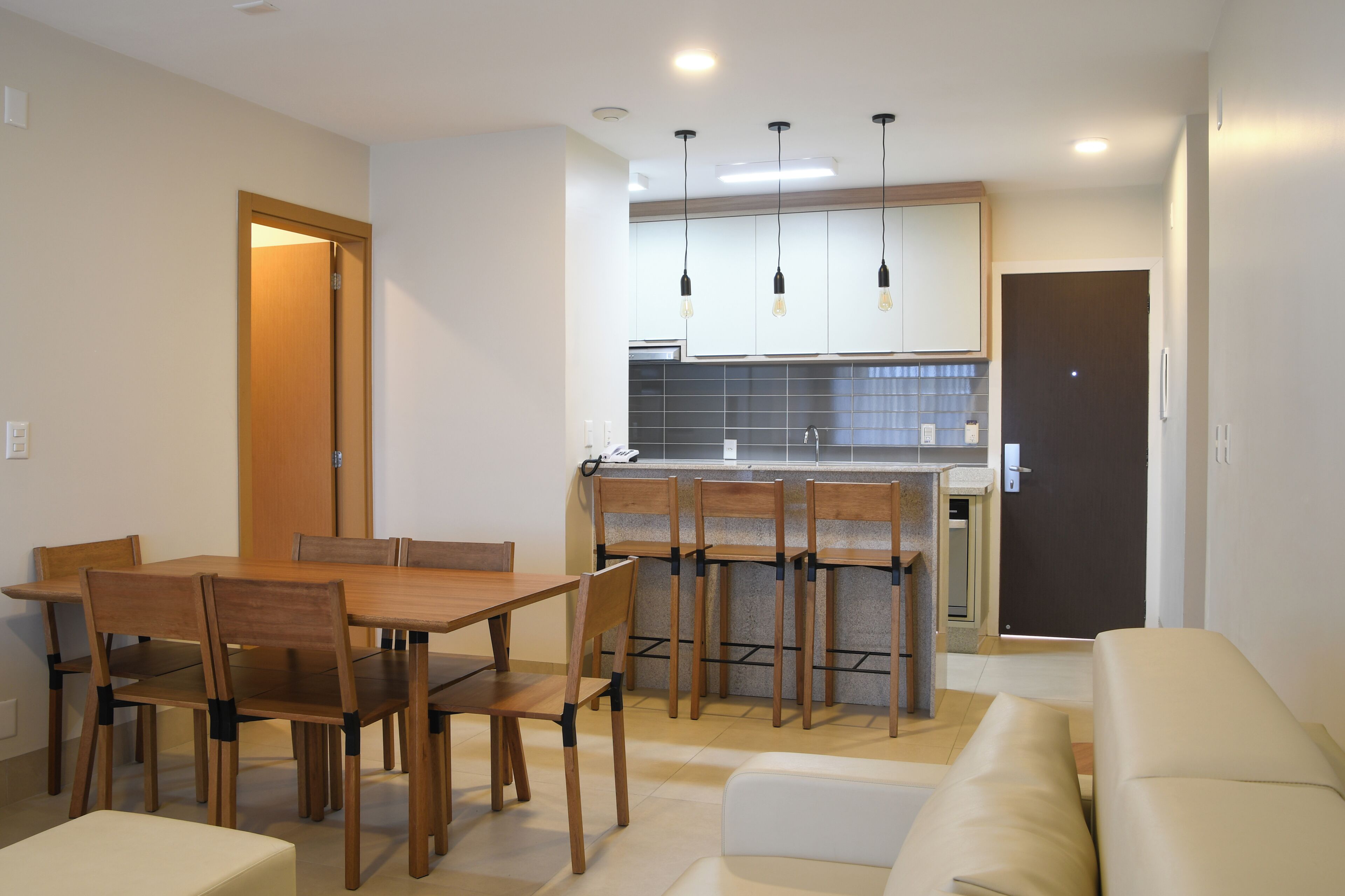A modern kitchen with wooden chairs, a dining table, and pendant lights.