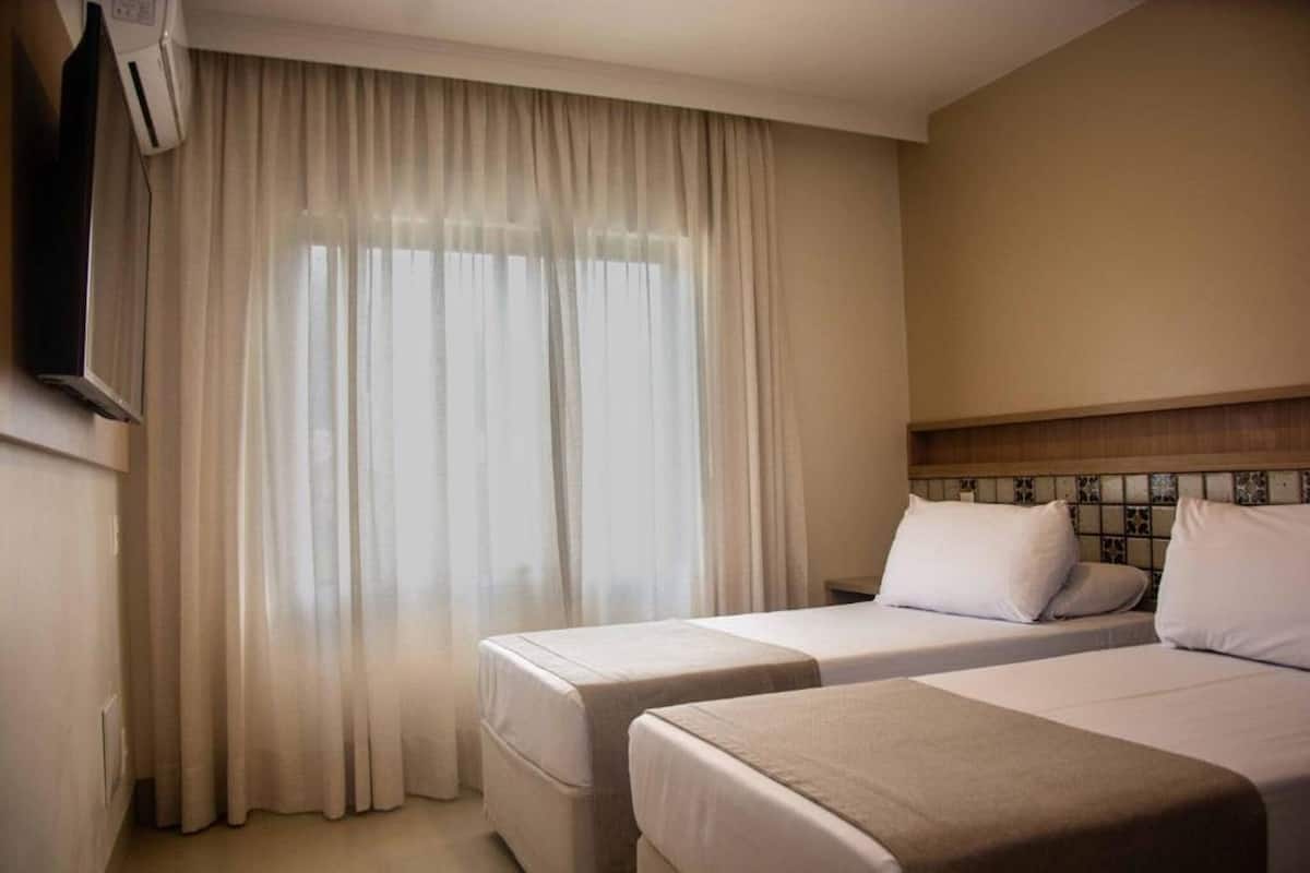 A hotel room with two beds, a TV, and a window with curtains.