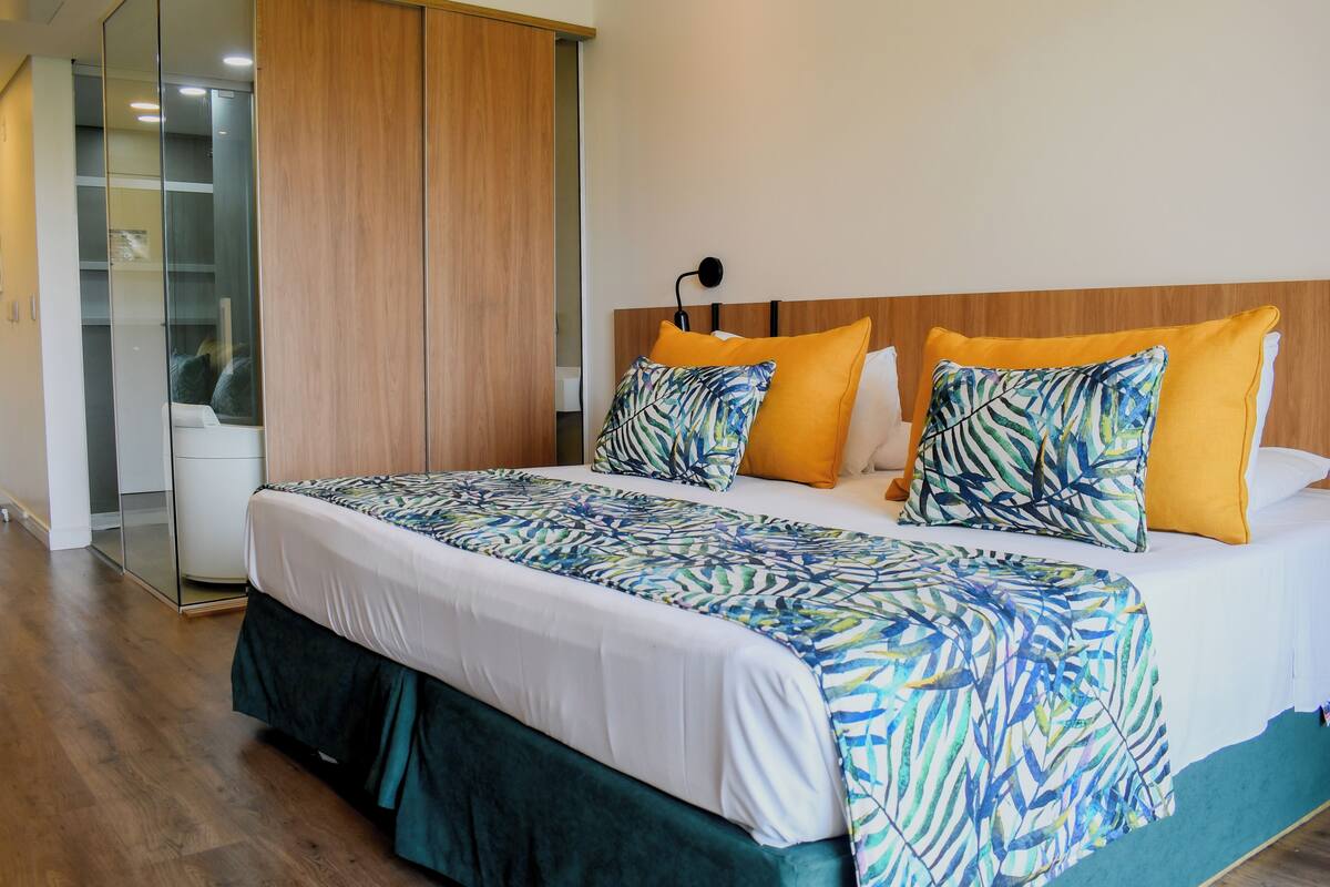 A hotel room with a large bed, a wooden headboard, a nightstand, and a wardrobe with a mirror.