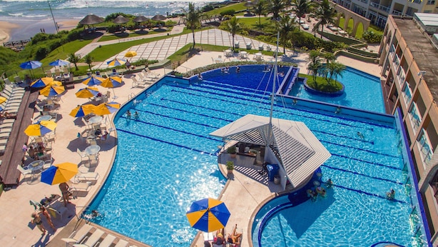 Une grande piscine extérieure avec plusieurs couloirs de nage, entourée de chaises longues et de parasols, et offrant une vue sur l’océan.