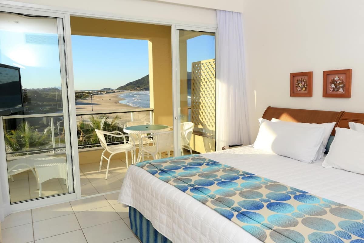 A hotel room with a bed, a balcony with a table and chairs, and a view of the beach.