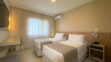 Quarto de hotel com duas camas, televisão, ar condicionado e mesa de cabeceira com telefone.