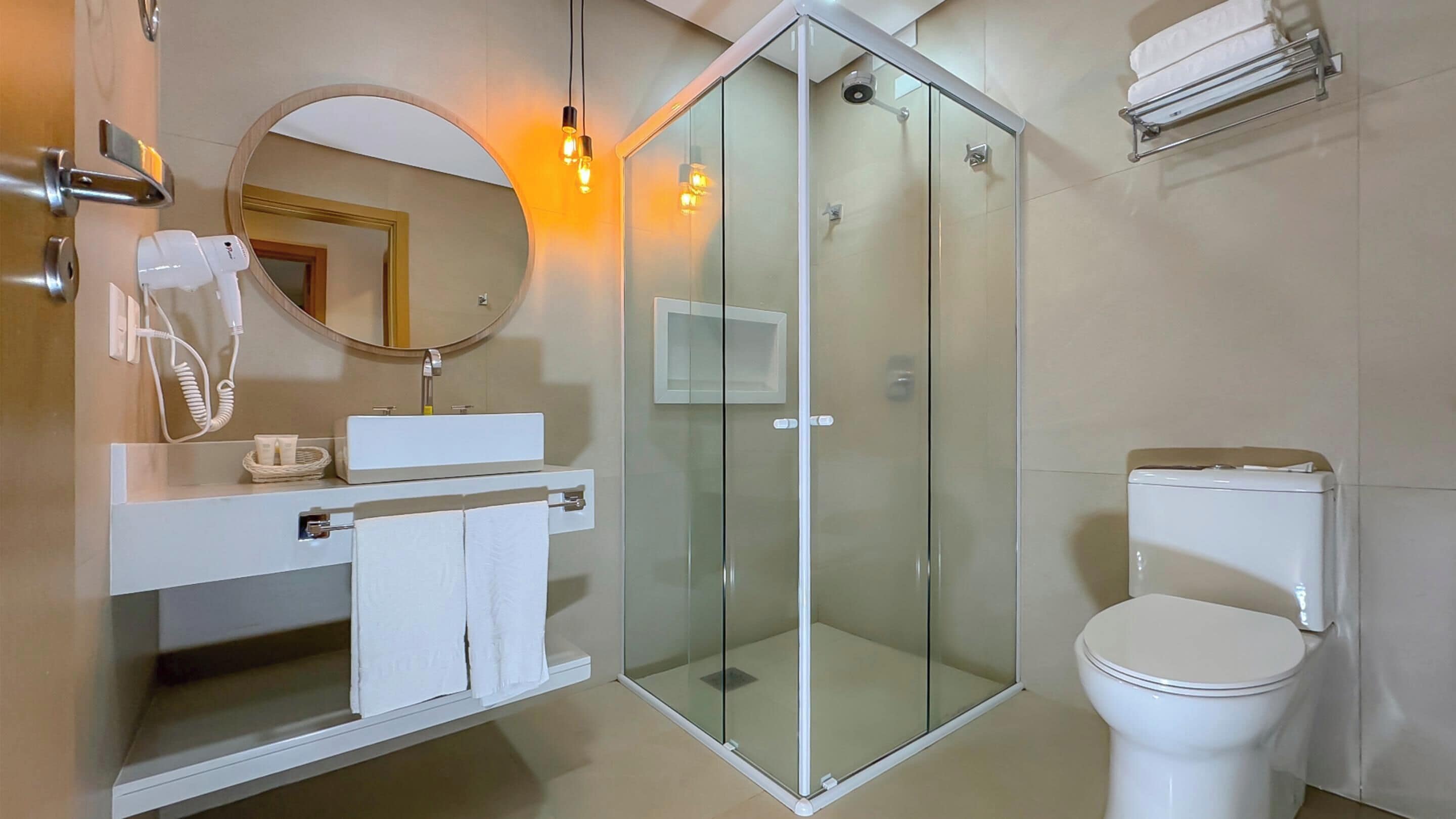 Uma casa de banho moderna com chuveiro de vidro, uma pia branca com espelho acima e sanita.