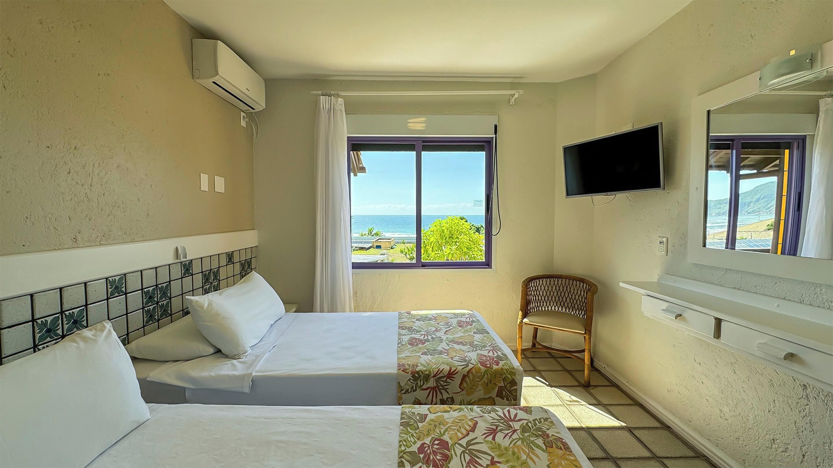 A hotel room with two beds, a TV, a chair, and a window with a view of the sea.