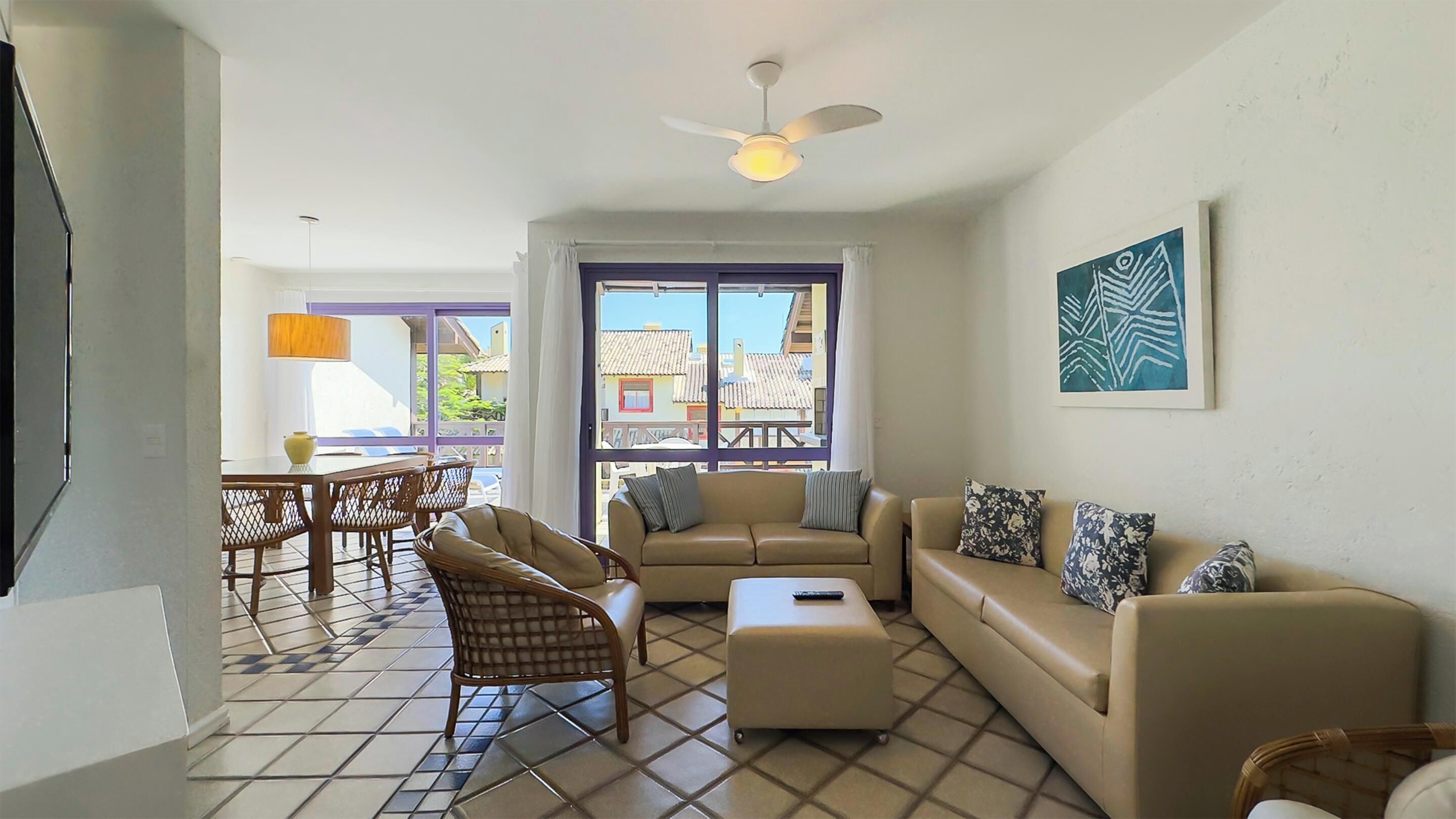 A living room with a sofa, ottoman, and wicker chairs. There is a ceiling fan, a table with a lamp, and a window with curtains. - Costao do Santinho Resort - All Inclusive (Florianópolis)