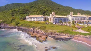 Un hôtel situé sur la côte, composé de plusieurs bâtiments, avec une plage et un paysage montagneux en arrière-plan.