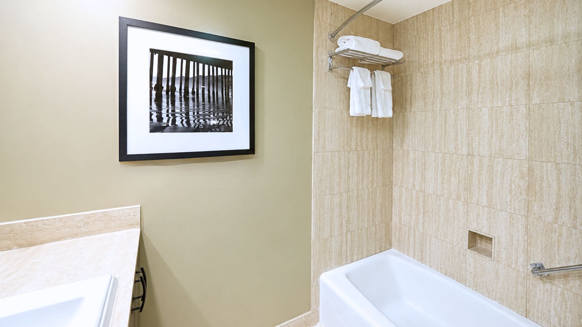 A bathroom with a bathtub, a framed picture on the wall, and a towel rack with towels.