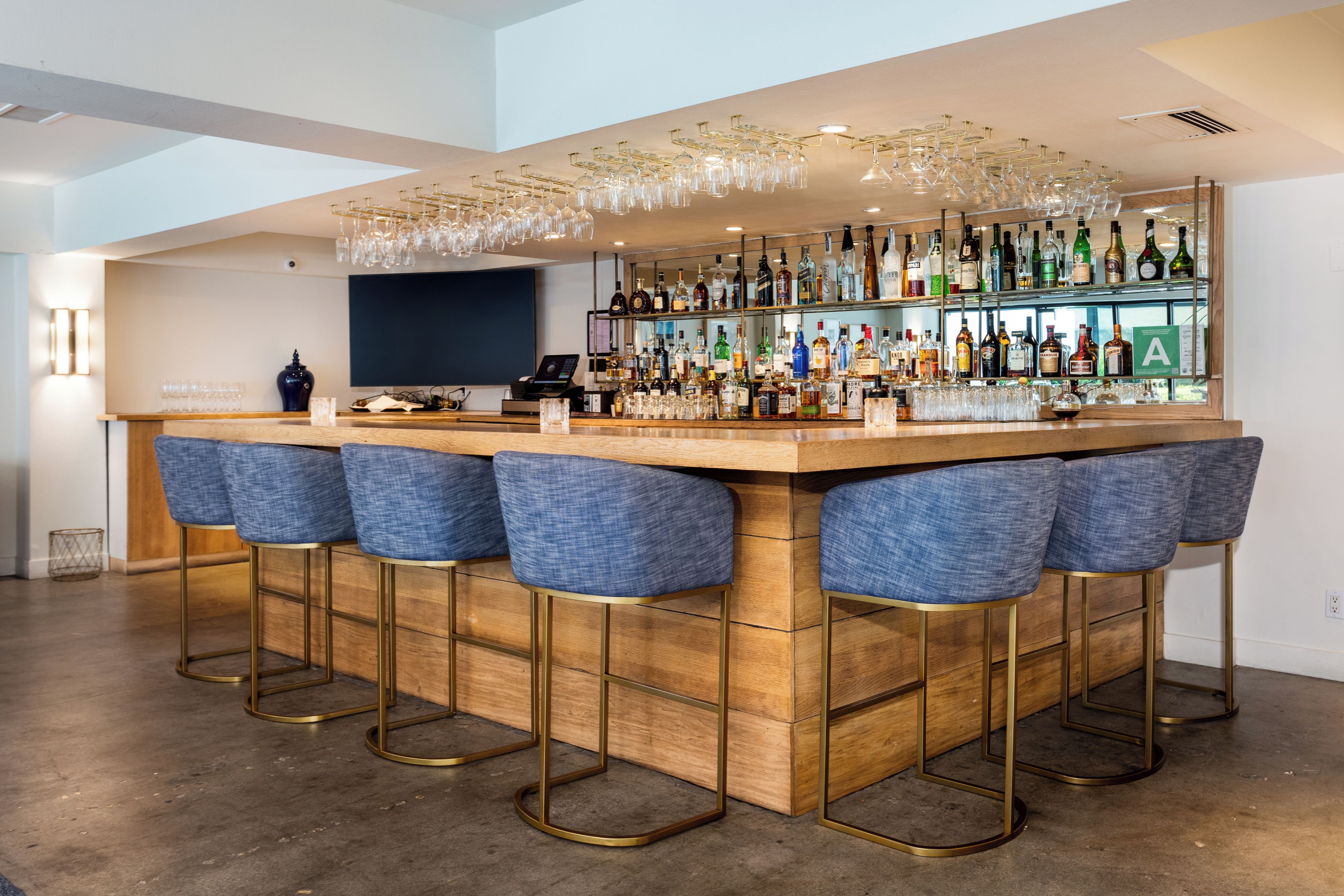 A bar area with a wooden counter, multiple stools, and a variety of bottles.