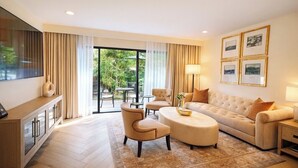 A modern living room with a sofa, armchairs, a coffee table, and a TV on a cabinet. There are curtains, a rug, and framed pictures on the wall. - Luxe Sunset Boulevard Hotel (Los Angeles)