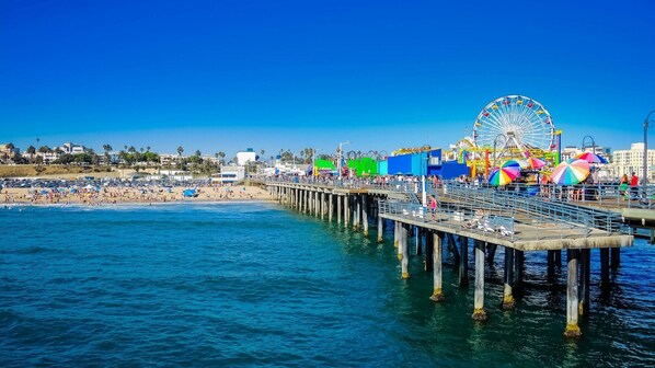 A pier extending into the ocean with a Ferris wheel and beach in the background.