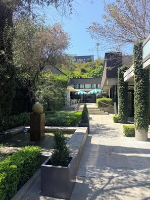 A courtyard with a water feature, potted plants, and outdoor seating under umbrellas. - Luxe Sunset Boulevard Hotel (Los Angeles)