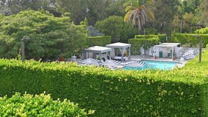 A pool area with lounge chairs and umbrellas, surrounded by well-maintained hedges and trees. - Luxe Sunset Boulevard Hotel (Los Angeles)