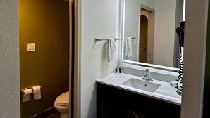 Een badkamer met een wit wastafelmeubel, een spiegel met verlichting, een toilet en een handdoekrek.