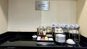 Een hotelkamer met een bordje 'Dream Cup', een koffiehoek met diverse dranken en keukengerei, en netjes gepresenteerd servies.