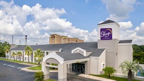 Een Sleep Inn by Choice Hotels met een modern ontwerp, met een centrale ingang, een overdekte doorgang, palmbomen en een parkeerplaats.