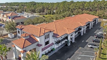 A multi-story building with a red-tiled roof, a parking lot, and a surrounding forested area.