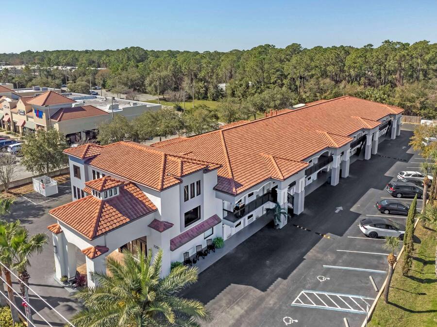 A multi-story building with a red-tiled roof, a parking lot, and a surrounding forested area.