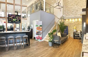 A modern hotel lobby with a bar area, a staircase, and a seating area. - Quality Inn Daytona Speedway I-95 (Daytona Beach)