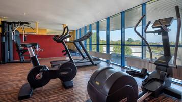 A gym with cardio machines, a weight bench, and large windows offering a view of the outdoors.