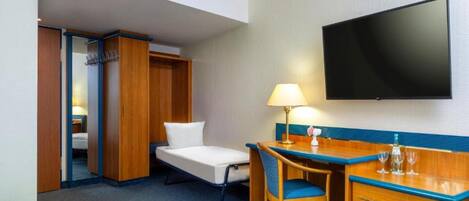 Una habitación de hotel con cama, escritorio, silla, televisor y armario.