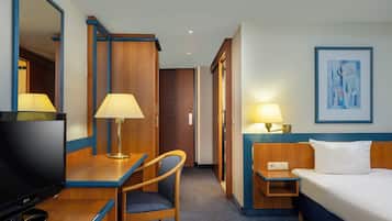 Una habitación de hotel con cama, escritorio, silla, televisor y dos lámparas de noche.